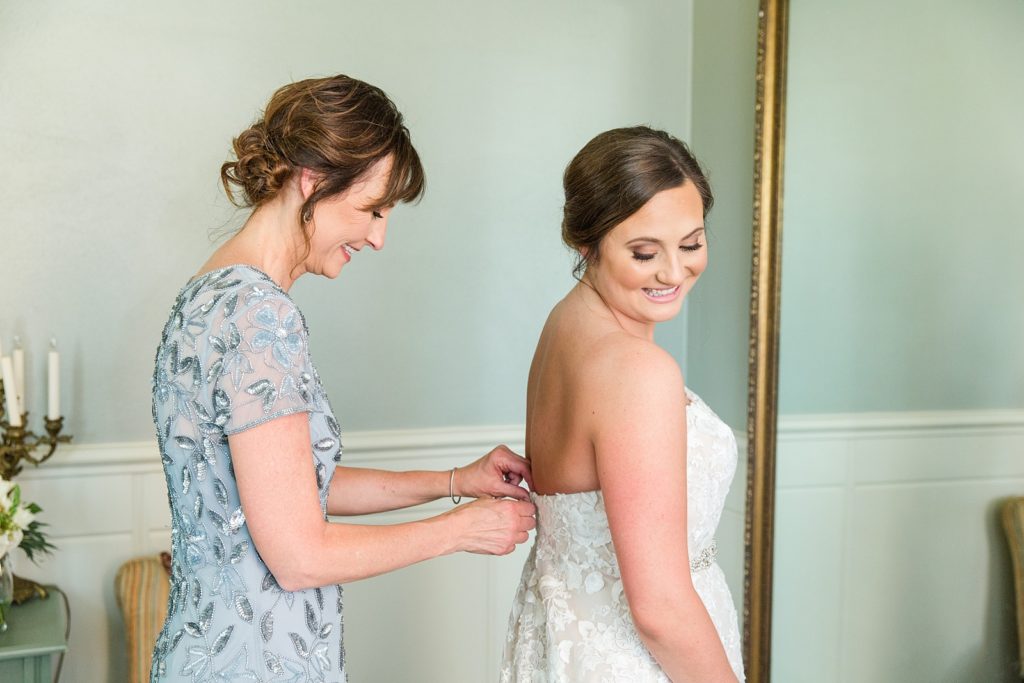Mother of the bride zipping bride's dress in front of mirror
