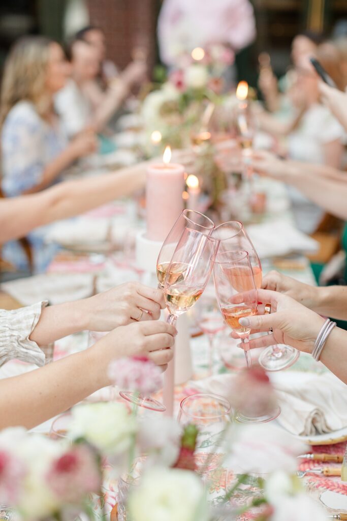 people clinking pink champagne glasses over table
